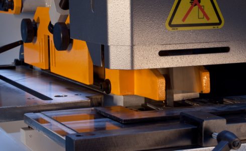 Steelworker mid-operation with only one station set up (e.g., punch station active) while other stations are clearly idle in-frame