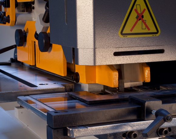 Steelworker mid-operation with only one station set up (e.g., punch station active) while other stations are clearly idle in-frame