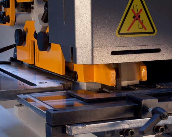 Steelworker mid-operation with only one station set up (e.g., punch station active) while other stations are clearly idle in-frame